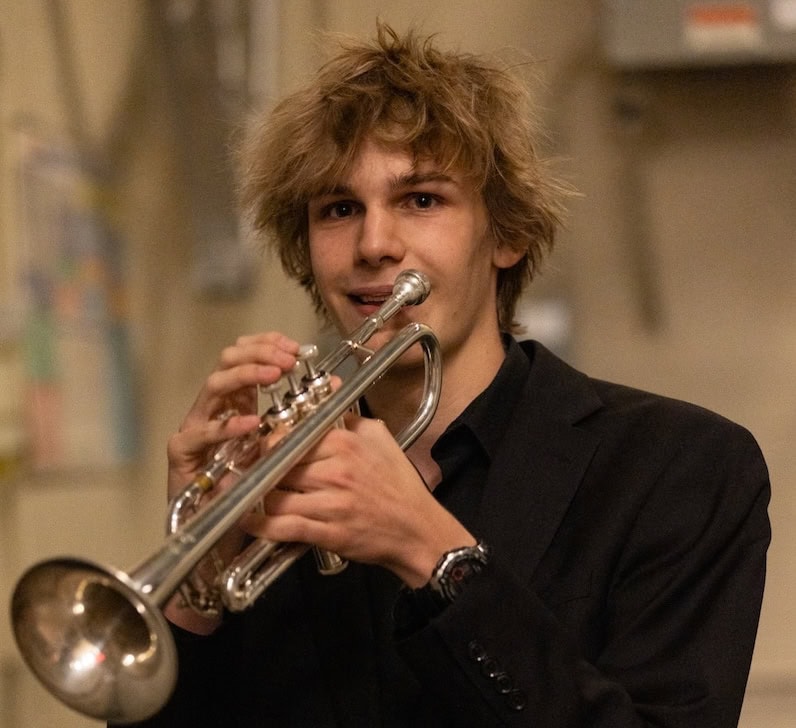 Student musician with a black suit playing a trumpet.