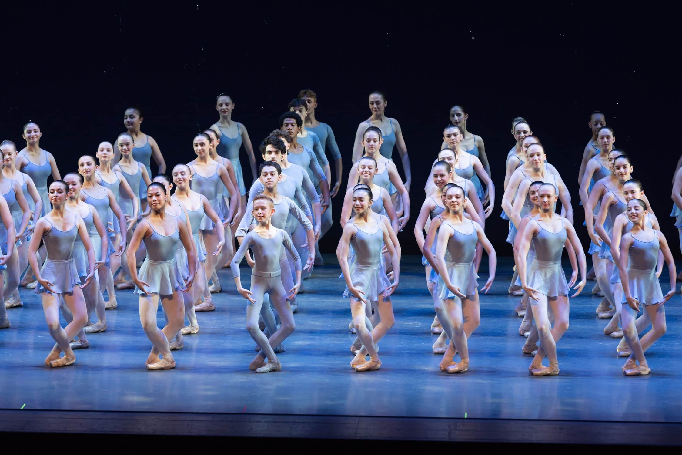 Many ballet dancers in rows and lines and light colored costumes.