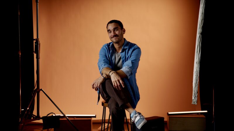 Adam Benavides, sitting in front of an orange background.