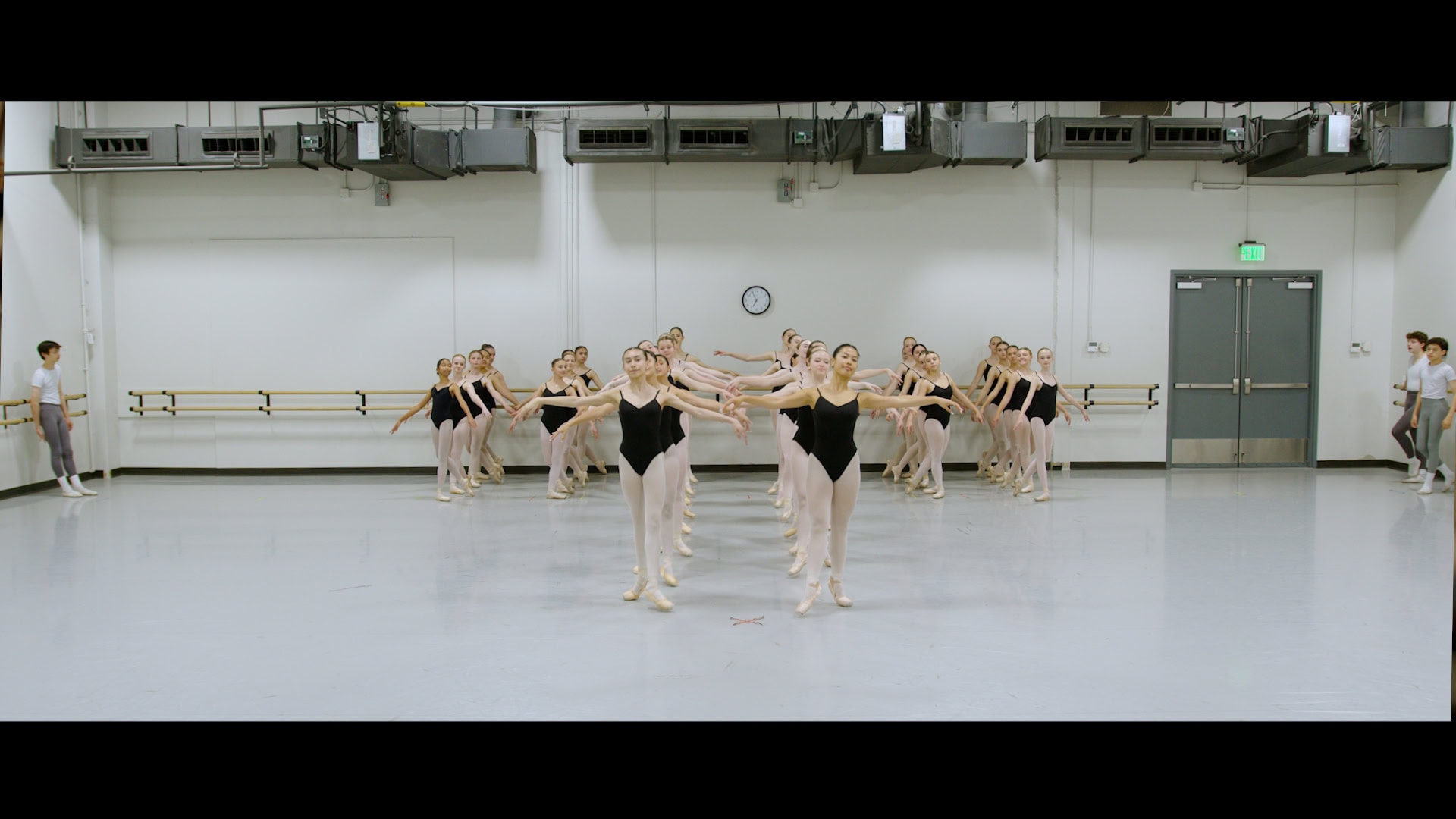 Ballet dancers rehearsing, wearing black tops and in a light colored room.